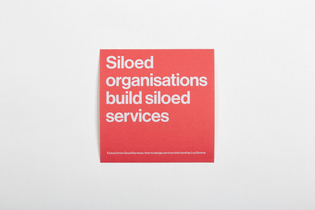 A bright orange square sticker with the words, "Siloed organizations build siloed services" in white type.